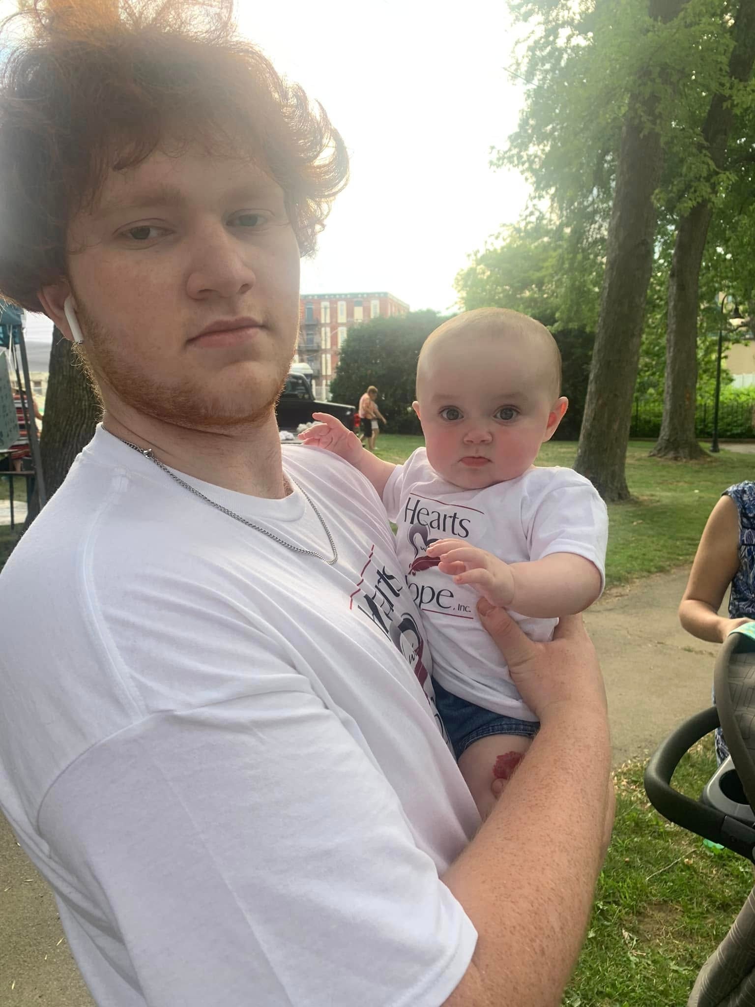 Person holding baby wearing Hearts with Hope shirts at outdoor park